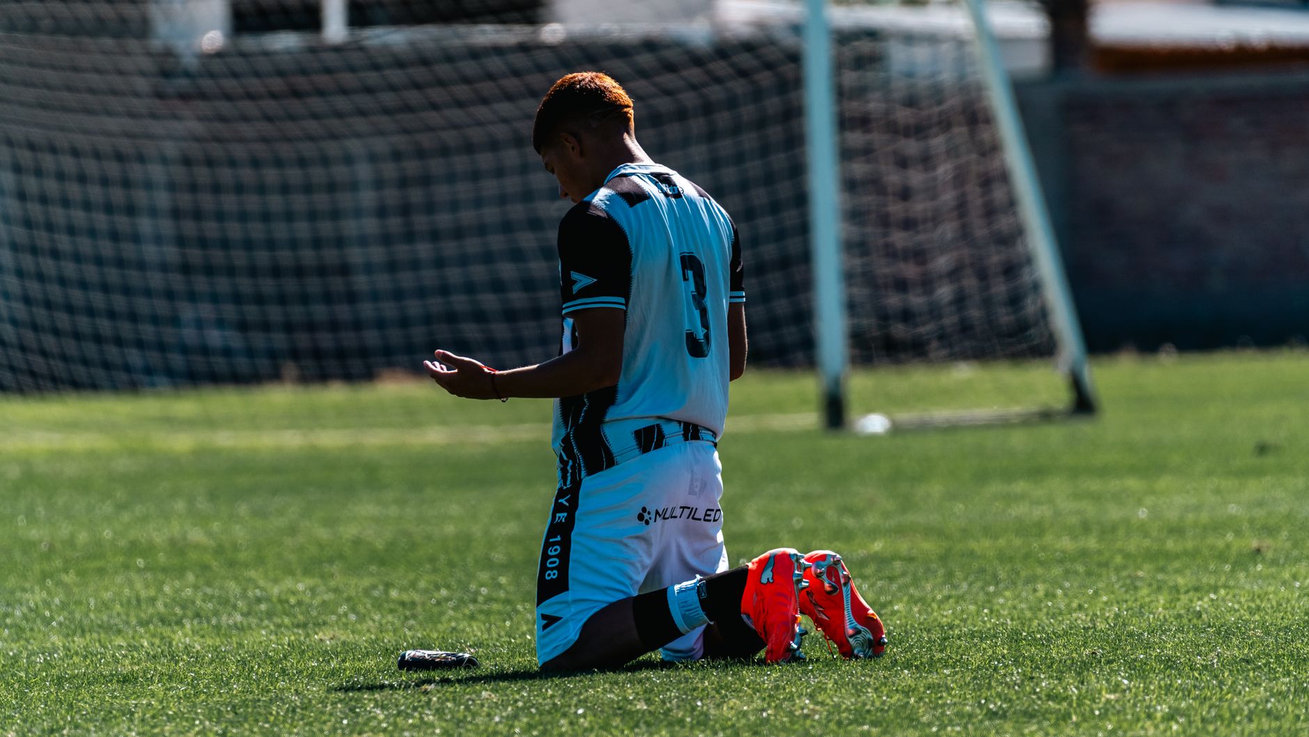 A soccer player kneels on the field, reflecting after a game, in a contemplative pose.